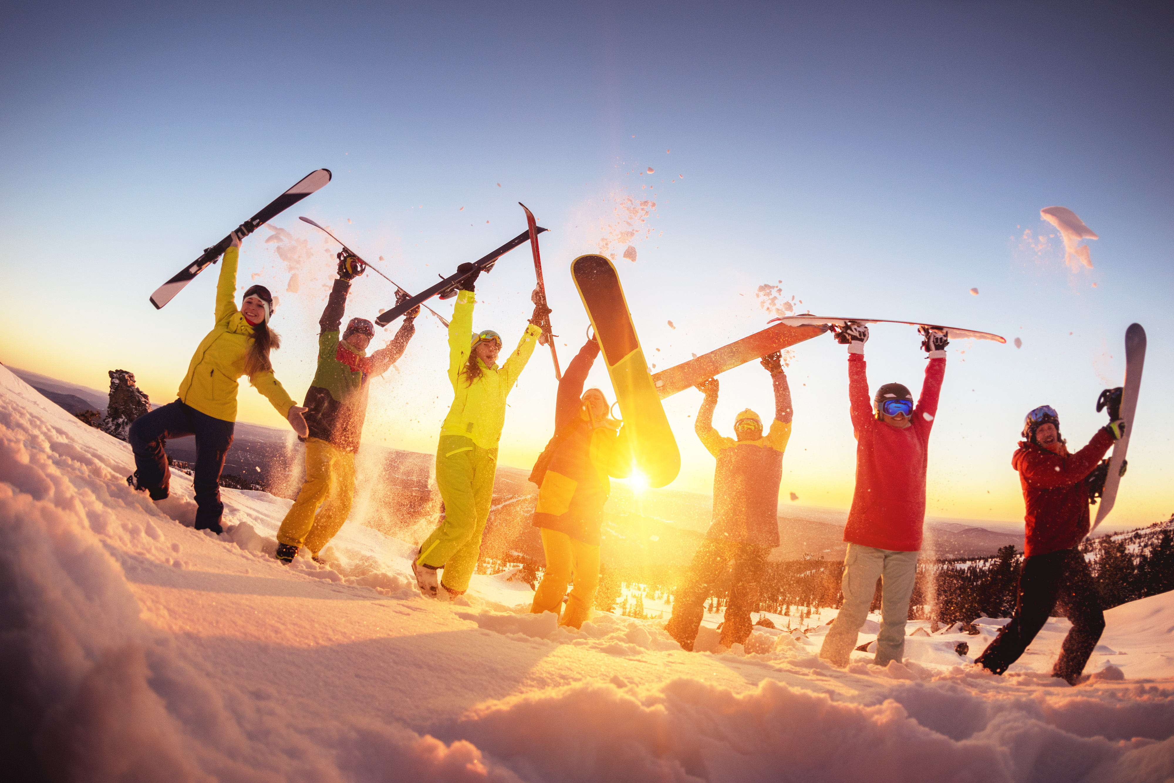 Group of happy friends skiers and snowboarders is having fun at ski resort against sunset